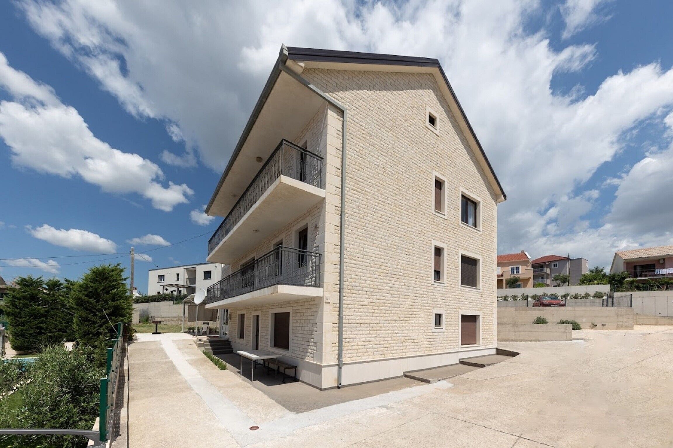 A modern two-story building with a flat roof, a balcony on the upper floor, and a small window on the lower floor.