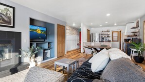 A modern living room with a flat-screen TV, a fireplace, a dining area, and a kitchen.