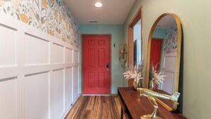 A hallway with a red door, a wooden bench, a mirror, and a decorative wall with floral wallpaper.