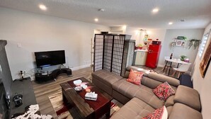 A living room with a sofa, a TV, a coffee table, and a kitchen area with a fridge and microwave. - Private Bachelor Unit close to St. Clair College walking distance  (Windsor)