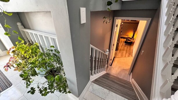 A staircase with a white railing, a potted plant, and a light switch on the wall. - Private Bachelor Unit close to St. Clair College walking distance  (Windsor)