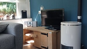 Een moderne woonkamer met een houten bureau, een zwarte flatscreen televisie, een witte verwarming en een grijze bank.