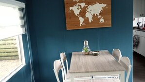 Een eetgedeelte met een houten tafel en witte stoelen, een wereldkaart aan de muur en een raam met luiken.