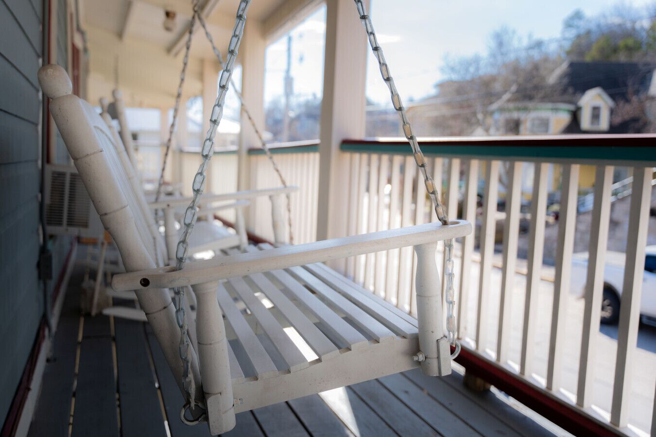 Une véranda avec des chaises en bois peintes en blanc et une balançoire.
