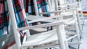 Een rij witte houten stoelen met geruite dekens, bevestigd aan een veranda met een houten balustrade.