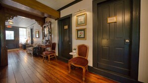 A wooden-floored hallway with a dark door, a small table with a chair, and a sofa. - Downtown Victorian St Piedmont (Eureka Springs)