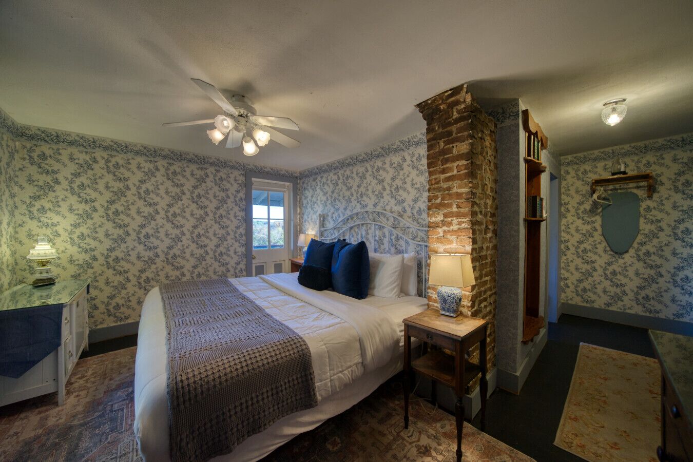 Une chambre à coucher avec un lit, une table de chevet, une lampe, une bibliothèque et une fenêtre.
