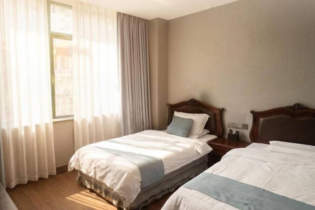 Una habitación de hotel con dos camas, una ventana con cortinas, un cabecero de madera y una mesita de noche.