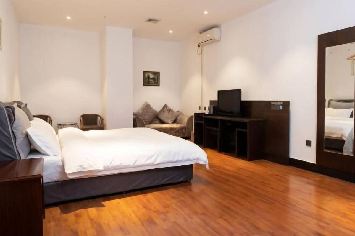 Un dormitorio con cama, televisión, espejo y suelo de madera.