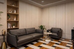 A modern living room with a sofa, a smaller armchair, a coffee table, and a bookshelf with decorative items. - Pandora Fashion Hotel (Yanji Yanbian University West Market Branch) (Yanji)
