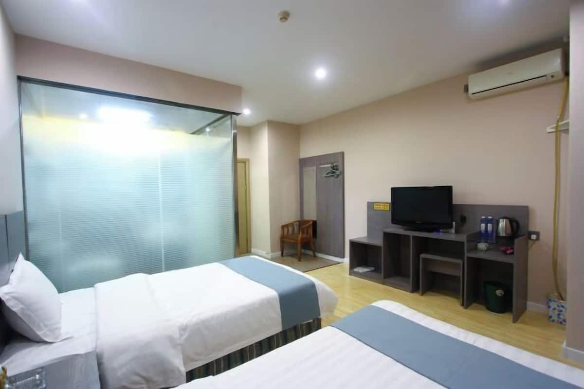 Habitación de hotel con dos camas, televisión, escritorio y aire acondicionado.