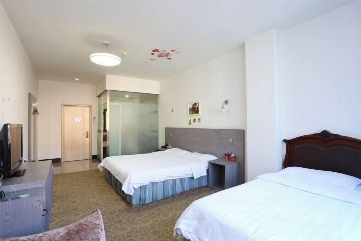 Habitación de hotel con dos camas, un escritorio, un televisor y una puerta que da a otra habitación.