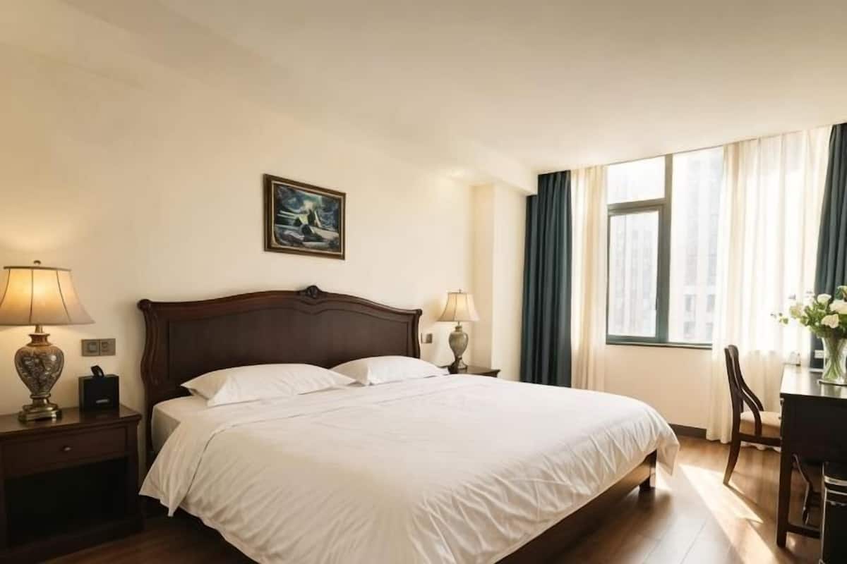 Una habitación de hotel con una cama grande, lámparas de noche, un escritorio con una silla y una ventana con cortinas.