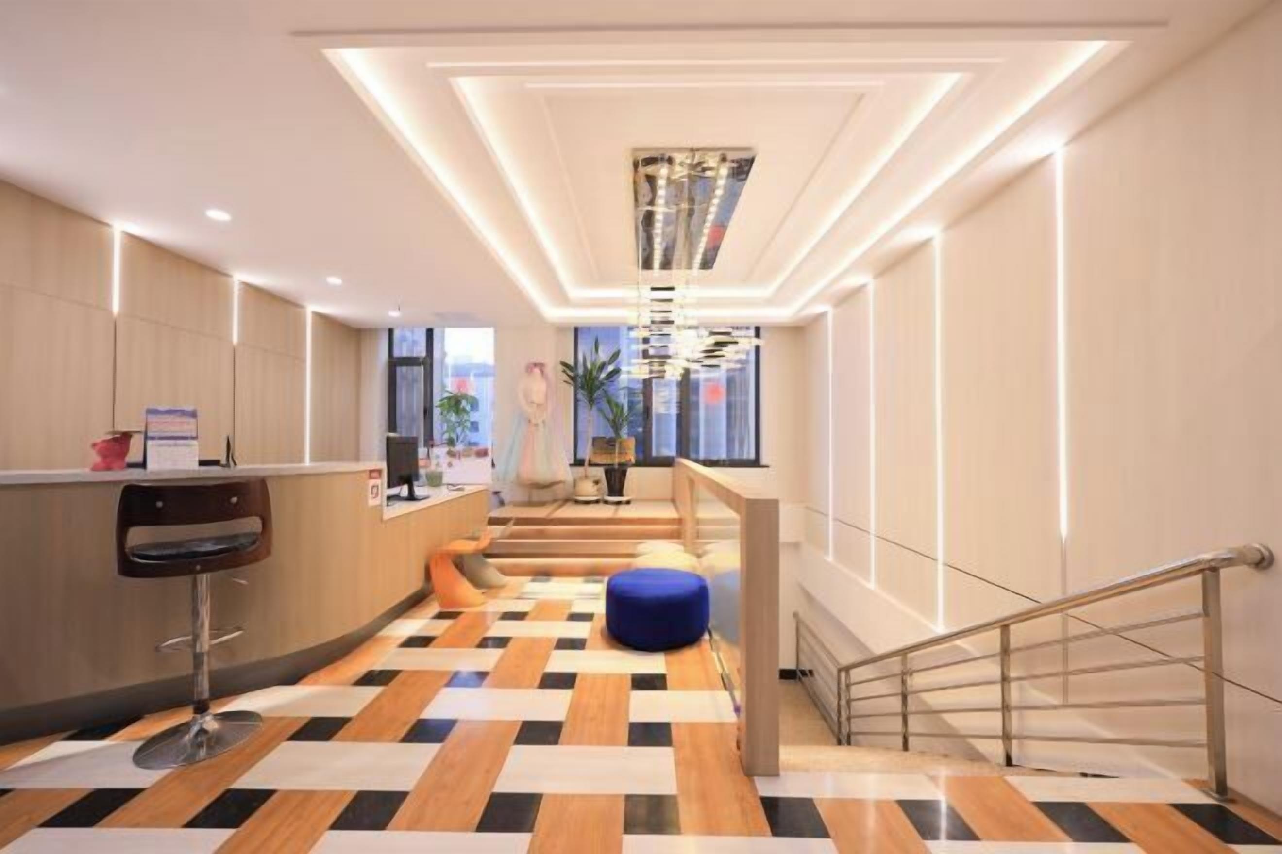 A modern hotel lobby with a check-in counter, a staircase, and a patterned floor.
