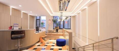 A modern hotel lobby with a check-in counter, a staircase, and a patterned floor.