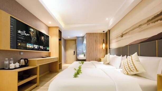 A modern hotel room with a large bed, a TV mounted on the wall, and a wooden desk with a kettle. - Taihe Kaida Business Hotel (Taihe People's Hospital) (Taihe)