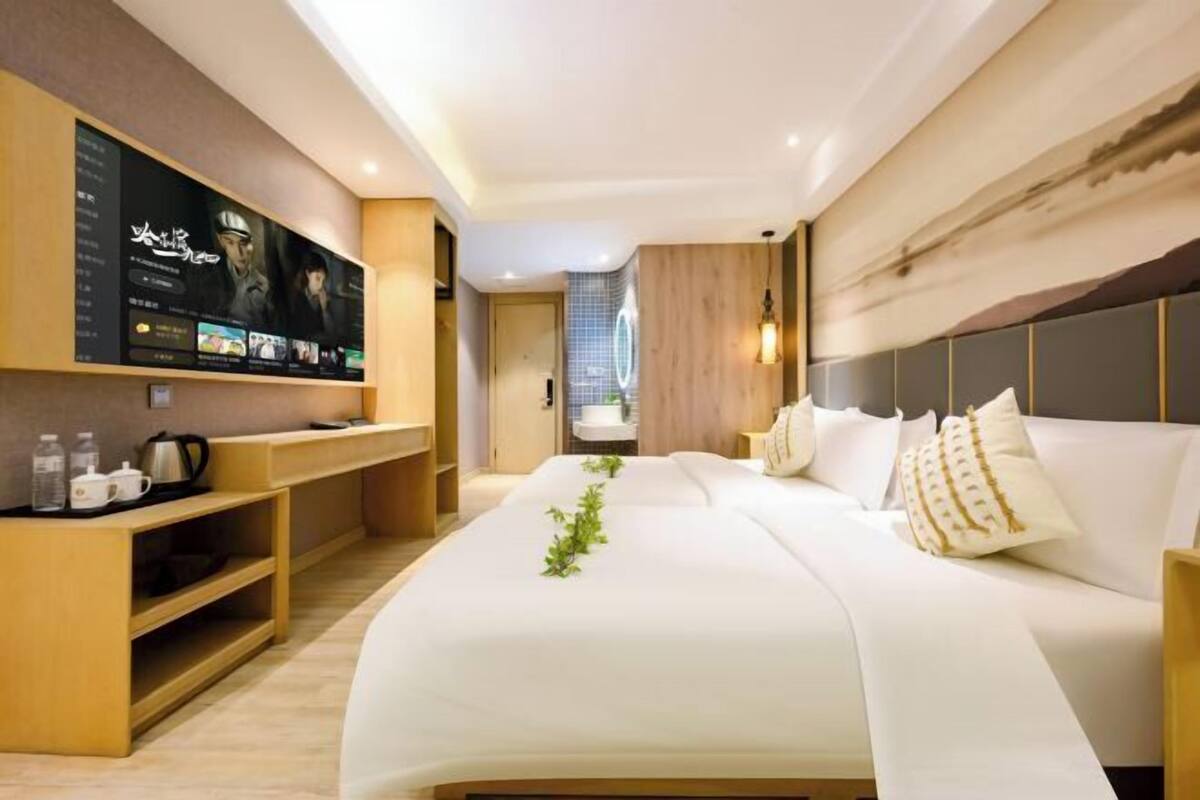 Une chambre d’hôtel moderne avec un grand lit, un téléviseur fixé au mur et un bureau en bois équipé d’une bouilloire.