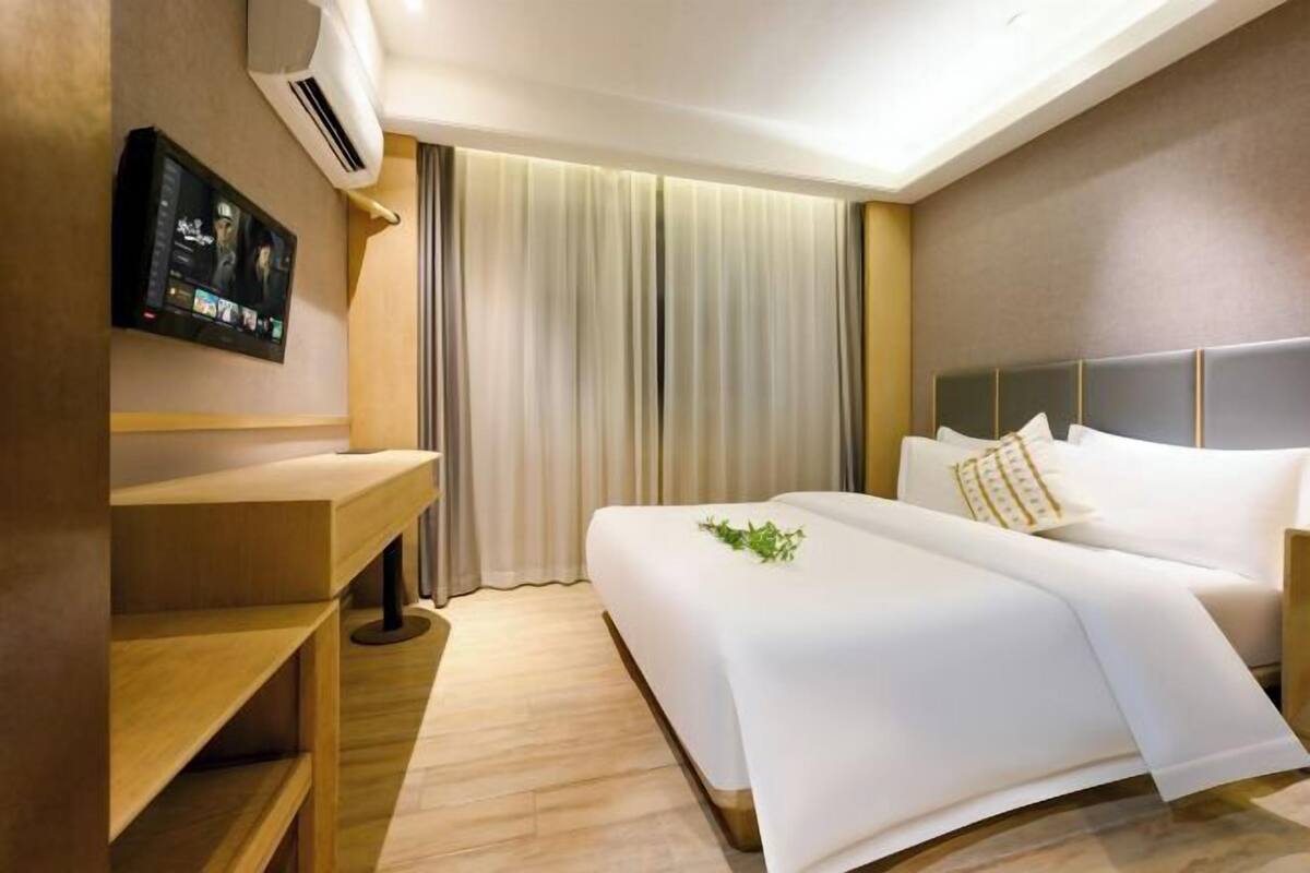 Une chambre d’hôtel avec un lit, un téléviseur fixé au mur, un bureau en bois et une fenêtre avec des rideaux.