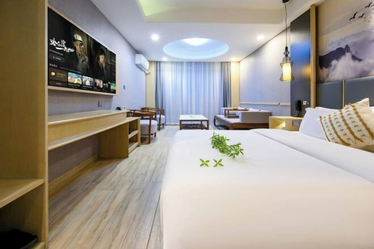 Une chambre d’hôtel avec un grand lit, un bureau, une chaise, une petite table et un téléviseur fixé au mur.