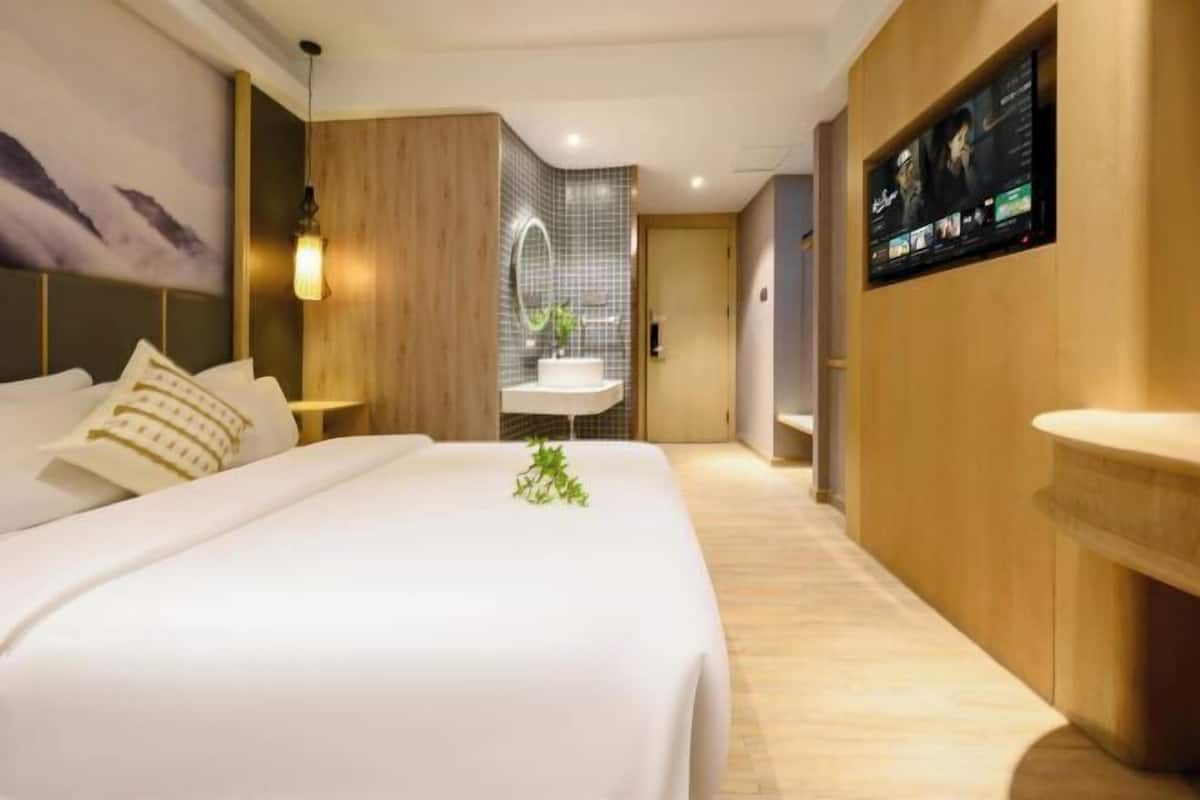 Une chambre d’hôtel avec un lit, une salle de bain dotée d’un miroir, d’un lavabo et d’un téléviseur fixé au mur.