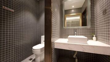 A modern bathroom with dark tiled walls, a white toilet, and a marble sink with a mirror above it.