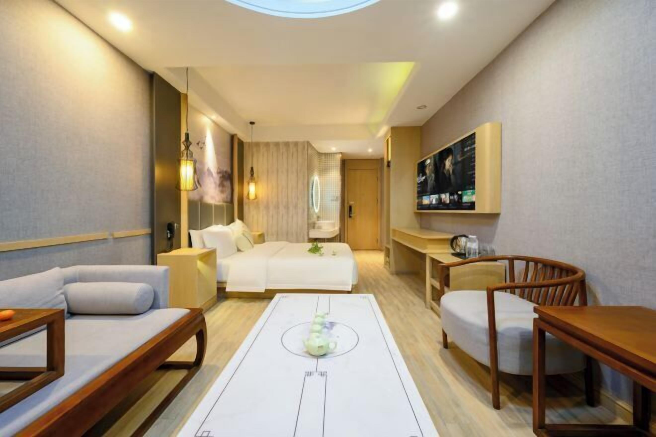 A modern hotel room with a sofa, a dining table, a TV, and a large window.