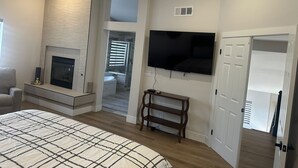 A bedroom with a large bed, a fireplace, a TV mounted on the wall, and a door leading to another room. - Charming 4-bedroom house in enchanting Las Vegas!  (Las Vegas)