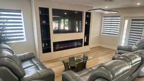 A modern living room with leather sofas, a glass coffee table, a flat-screen TV, and built-in shelves. - Charming 4-bedroom house in enchanting Las Vegas!  (Las Vegas)