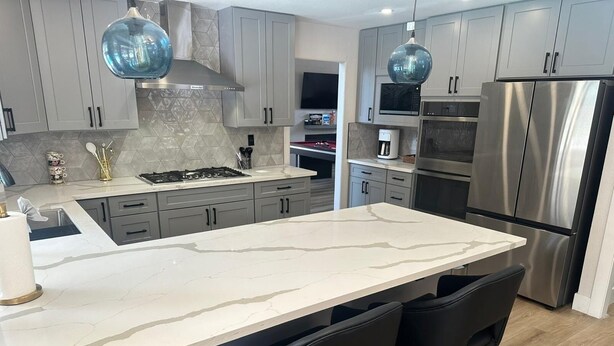 A modern kitchen with grey cabinets, a large island with bar stools, stainless steel appliances, and pendant lighting. - Charming 4-bedroom house in enchanting Las Vegas!  (Las Vegas)