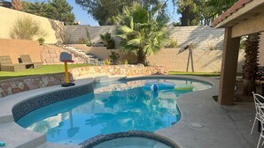 A swimming pool with a hot tub, surrounded by a stone wall and palm trees. - Charming 4-bedroom house in enchanting Las Vegas!  (Las Vegas)