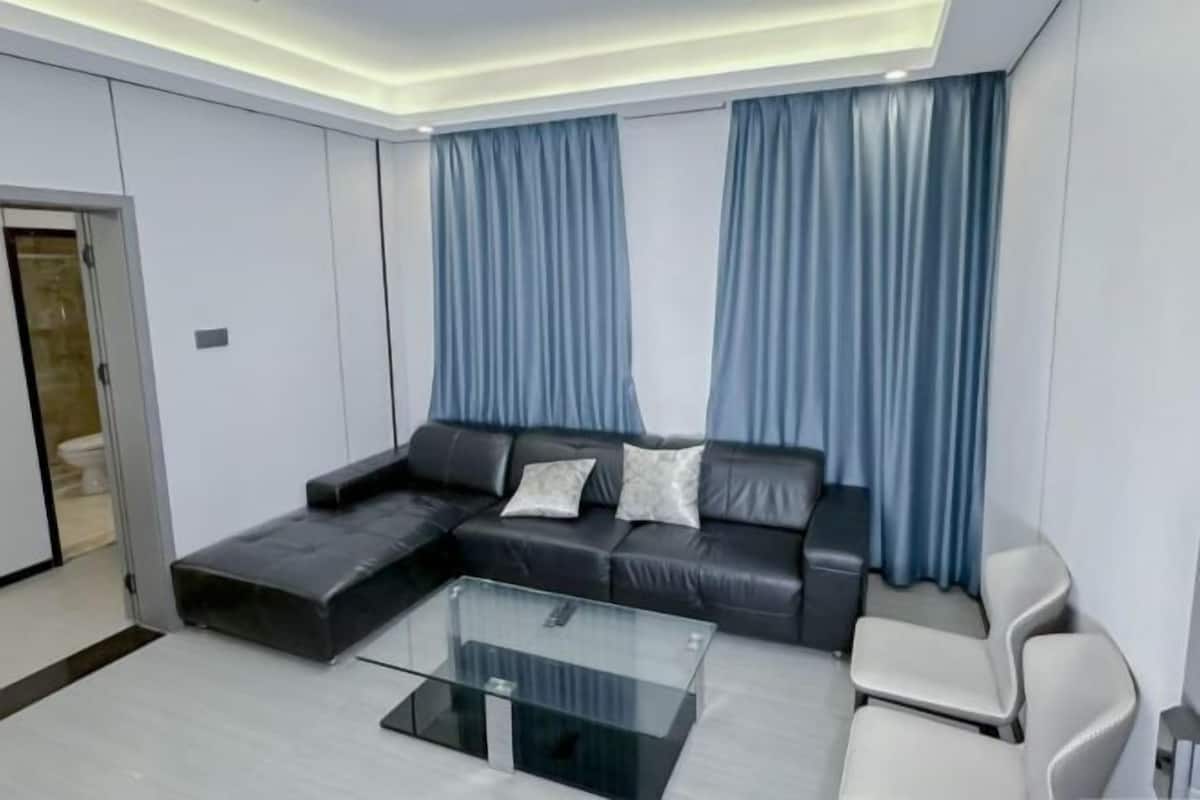 Un salon moderne avec un canapé d’angle, une table basse en verre et un fauteuil blanc.