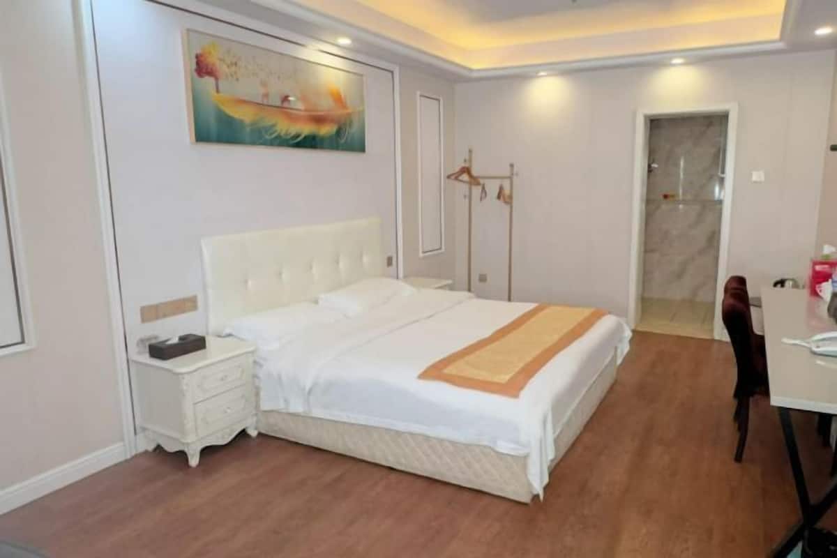 Une chambre à coucher avec un grand lit, une table de chevet, une armoire, un tableau au mur et une porte de salle de bain.