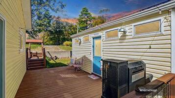 Uma casa móvel com deck de madeira, porta azul e um pequeno alpendre com cadeira e mesa.