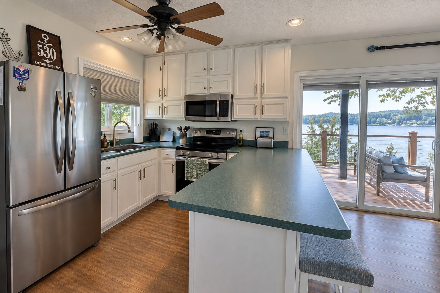 A modern kitchen with a large island, stainless steel appliances, and a view of a lake through the sliding glass door.