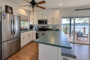 Una cocina moderna con una isla grande, electrodomésticos de acero inoxidable y vista a un lago a través de puertas corredizas de vidrio.