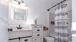 A bathroom with a white vanity, a toilet, a shower curtain with a geometric pattern, and a mirror above the vanity. - Lakefront Retreat •  King Suite • Covered Deck • Firepits • Sleeps 8 (Falls of Rough)
