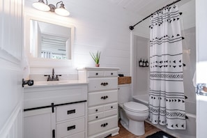 A bathroom with a white vanity, a toilet, a shower curtain with a geometric pattern, and a mirror above the vanity.
