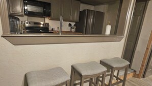 Une cuisine dotée d’un bar intégré, de tabourets en bois et d’un réfrigérateur en acier inoxydable.