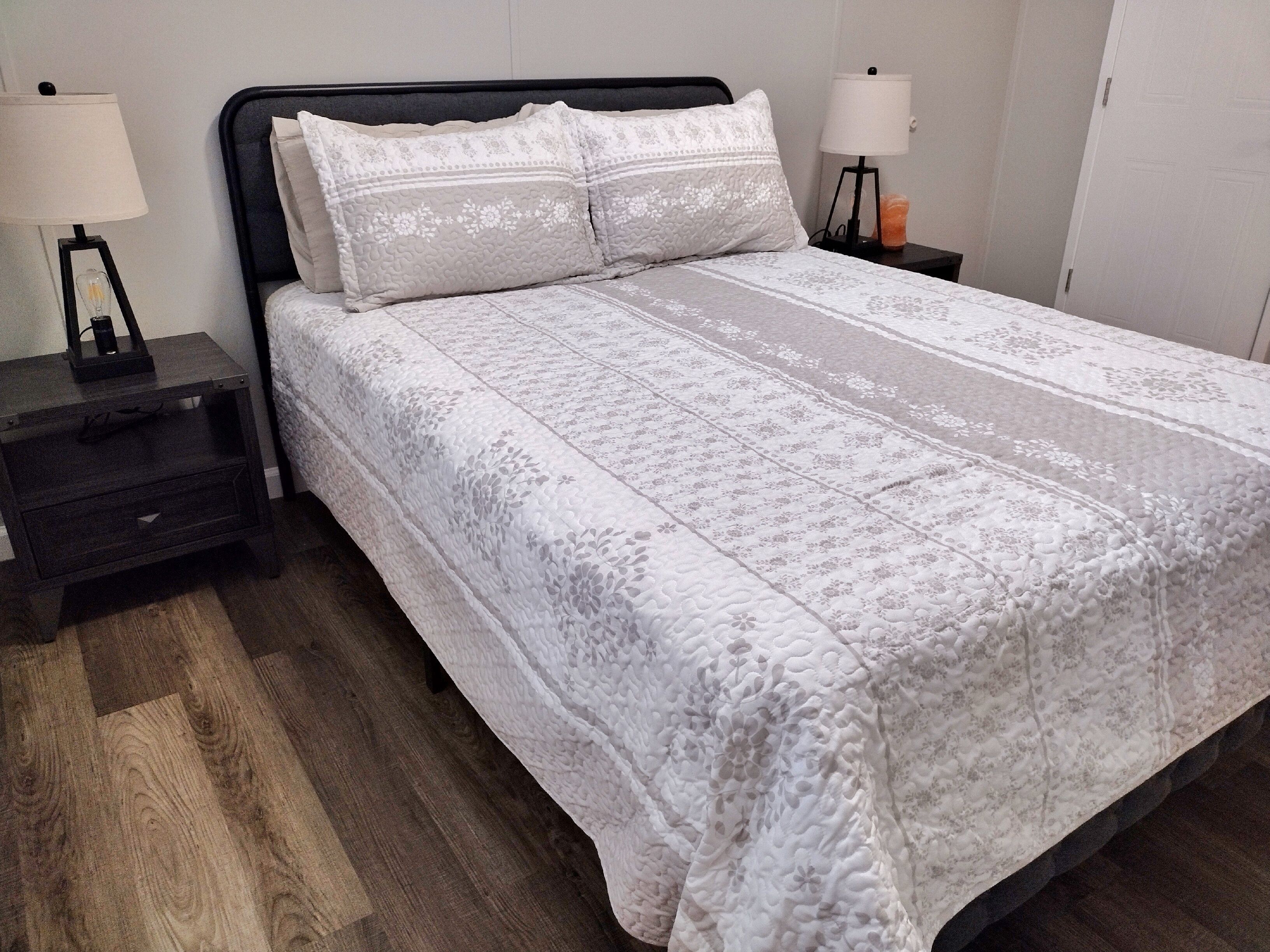 A neatly made bed with a floral patterned bedspread and two pillows, flanked by nightstands with lamps and a small candle.