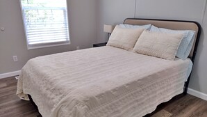 Une chambre à coucher comprenant un lit, une table de chevet, une fenêtre avec des stores et une prise électrique au mur.