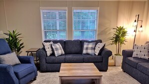 Un salon avec un canapé gris foncé, deux fauteuils, une table basse en bois et un tapis à motifs.