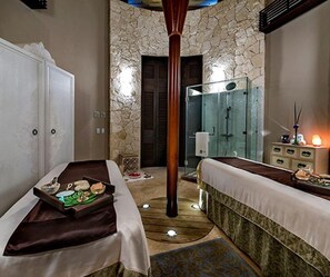 Une chambre d’hôtel avec deux lits, un mur en pierre, une douche et une table de chevet avec une lampe.