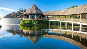 A resort with a thatched-roof structure, a bridge over water, and a reflection in the water. - 2BR Grand Luxxe Residence loft RM (Playa del Carmen)