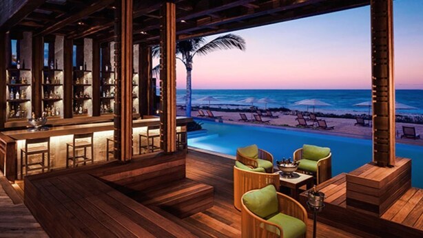 A wooden deck with a pool, lounge chairs, and a bar area with shelves of bottles. - 2BR Grand Luxxe Residence loft RM (Playa del Carmen)