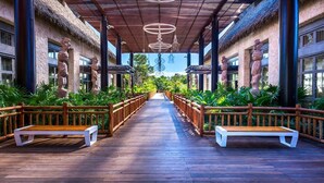 A wooden pathway flanked by benches and tropical plants, leading to a covered area with stone pillars and hanging lights. - 2BR Grand Luxxe Residence loft RM (Playa del Carmen)