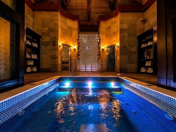Une piscine éclairée de lumières bleues, entourée de murs en pierre et de poutres en bois.