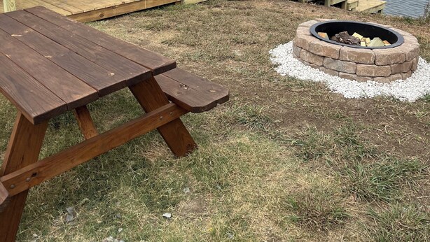 A wooden deck with a picnic table and a fire pit, overlooking a calm lake. - Bass Lodge - Lakefront - New (Commerce)