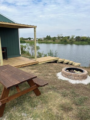 A wooden deck with a picnic table and a fire pit, overlooking a calm lake.