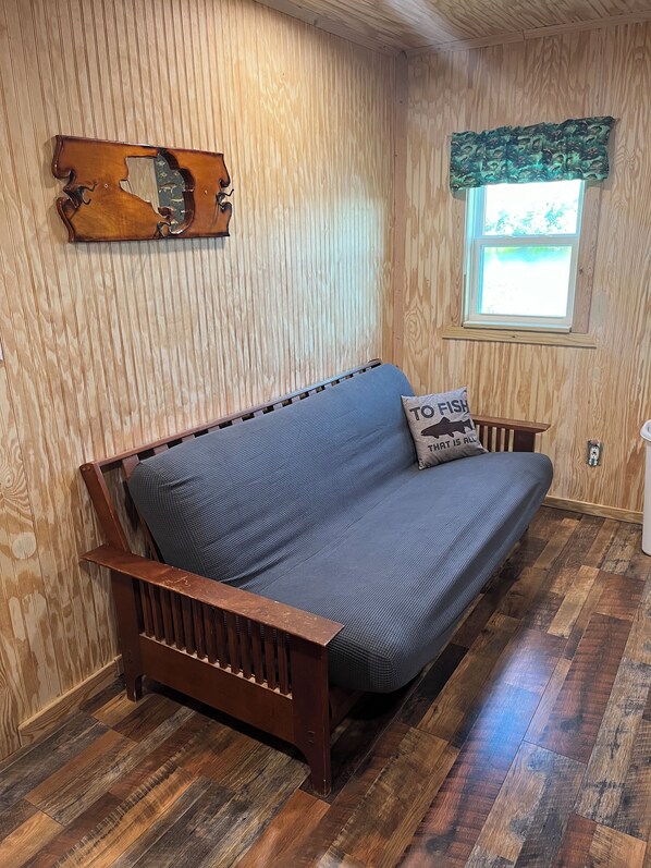 A wooden-paneled room with a wooden bench, a window with a green valance, and a cushion with "TO FISH" text.