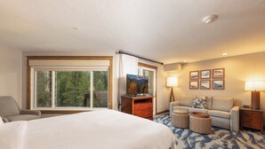 Une chambre d’hôtel avec un grand lit, un canapé, une télévision, un bureau et une fenêtre donnant sur des arbres.